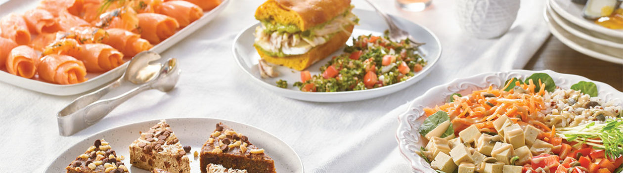 Grande table avec produits frais: sandwichs, salades et rouleaux de saumon fumé.
